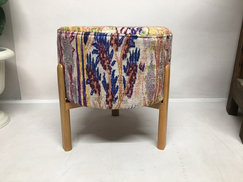 May include: A round, upholstered ottoman with a colorful floral pattern in shades of blue, red, and yellow. The ottoman has four wooden legs.