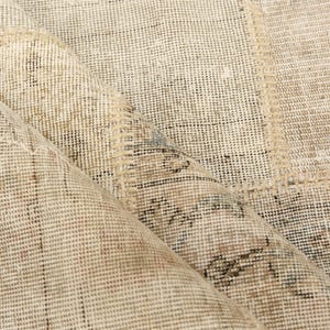 Könnte beinhalten: Nahaufnahme eines beige-braunen gemusterten Teppichs mit einem abgenutzten, Vintage-Aussehen. Der Teppich hat ein Patchwork-Design mit sichtbaren Nähten und einer gewebten Textur. Die Farbpalette umfasst Beige-, Braun- und Schwarztöne.