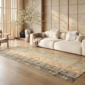 May include: A rectangular area rug with a faded, patterned design in neutral tones of beige, gray, and yellow. The rug is placed on a hardwood floor in a living room setting, with a white sofa and decorative elements in the background.
