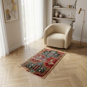 Puede incluir: Una alfombra rectangular con un complejo patrón geométrico en tonos rojo intenso, verde azulado y crema. La alfombra tiene una textura desgastada con flecos visibles en los bordes cortos, mostrando un diseño simétrico con motivos lineales.