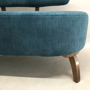 May include: A teal blue fabric sofa with wooden legs. The sofa has a rounded back and a curved seat.