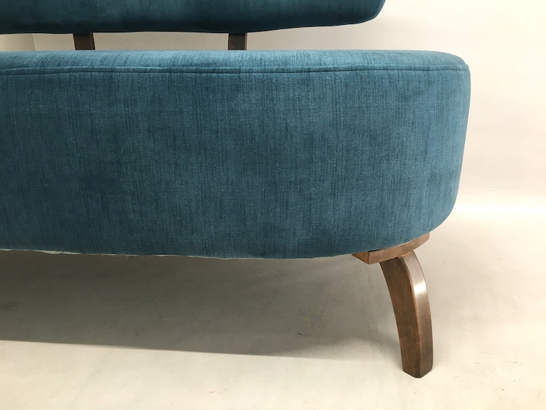 May include: A teal blue fabric sofa with wooden legs. The sofa has a rounded back and a curved seat.