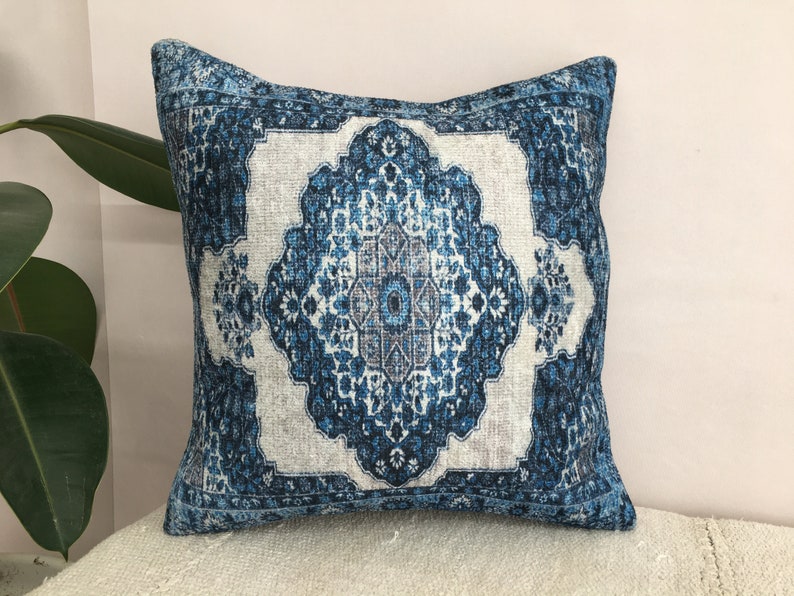 Op de afbeelding: Vierkant decoratief kussen met een blauw en wit patroon. Het kussen heeft een centraal medaillonontwerp met bloem- en geometrische elementen. Het kleurenpalet omvat tinten blauw, wit en grijs, wat een vintage esthetiek cre&euml;ert.