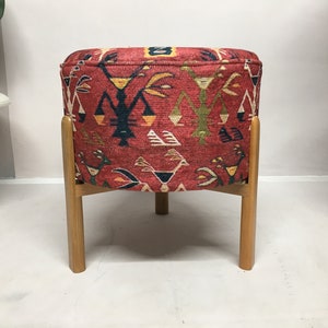 Puede incluir: Un otomano redondo con un patr&oacute;n rojo y negro y un marco de madera. El otomano tiene una parte superior redonda y cuatro patas.