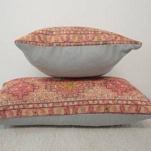 May include: Two decorative throw pillows with a patterned fabric featuring a geometric design in shades of pink, red, yellow, and blue. The pillows have a light gray backing.