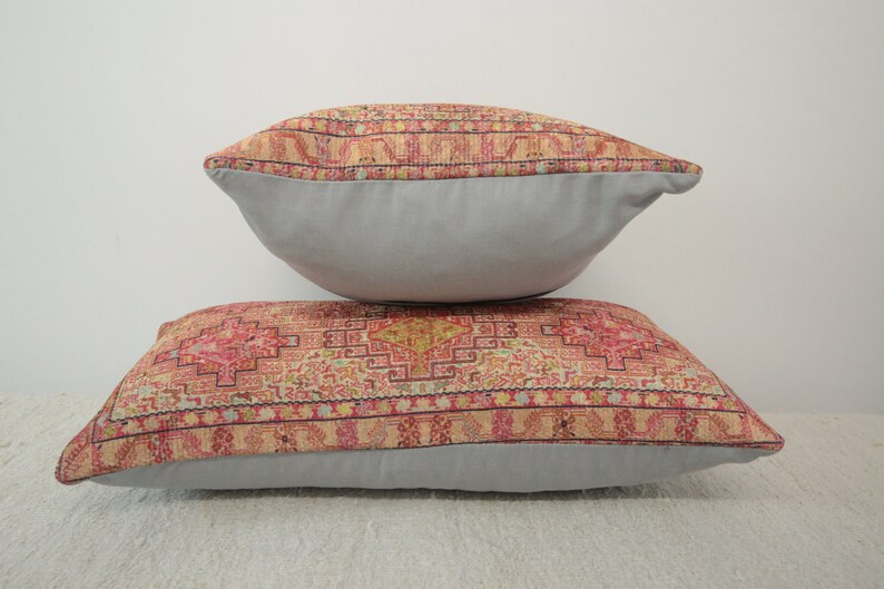 May include: Two decorative throw pillows with a patterned fabric featuring a geometric design in shades of pink, red, yellow, and blue. The pillows have a light gray backing.