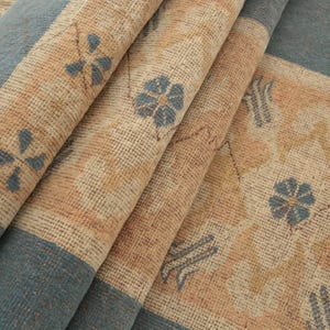 K&ouml;nnte beinhalten: Nahaufnahme eines gefalteten Teppichs mit einem blauen und beigen Muster. Der Teppich hat ein florales Design mit blauen Blumen auf einem beigen Hintergrund. Der Teppich ist in drei Teile gefaltet, wobei die blaue Seite nach au&szlig;en zeigt.