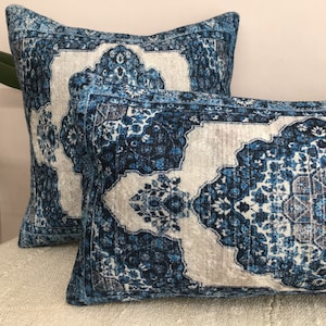 Op de afbeelding: Twee decoratieve kussens met een blauw en wit patroon. De kussens hebben een rechthoekige en vierkante vorm. Het patroon lijkt op een traditioneel tapijtontwerp, met ingewikkelde bloemen en geometrische elementen.