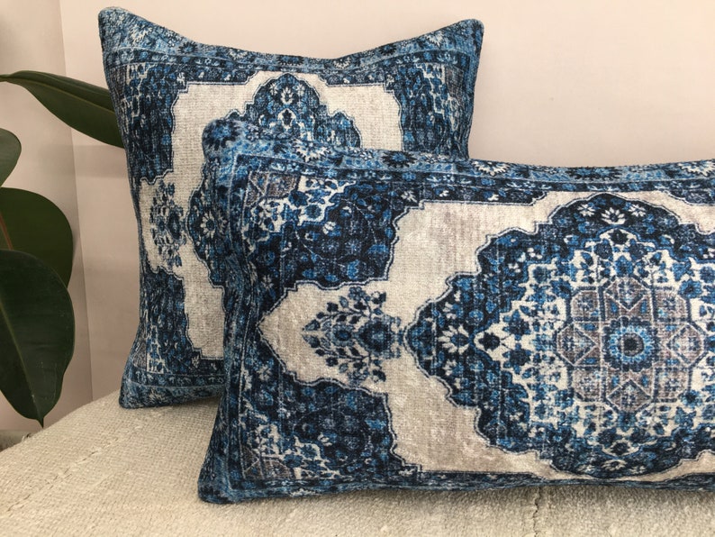 Op de afbeelding: Twee decoratieve kussens met een blauw en wit patroon. De kussens hebben een rechthoekige en vierkante vorm. Het patroon lijkt op een traditioneel tapijtontwerp, met ingewikkelde bloemen en geometrische elementen.