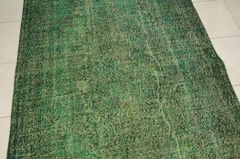 K&ouml;nnte beinhalten: Ein gr&uuml;ner Vintage-Teppich mit einem abgenutzten Look und einem dezenten Muster. Der Teppich hat ein verblichenes, abgenutztes Aussehen, das ihm einen einzigartigen Charakter verleiht.