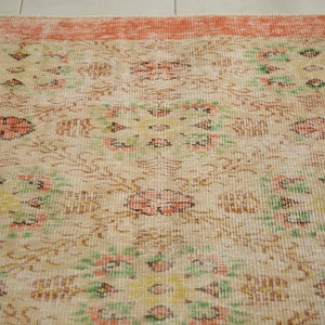 May include: A vintage rug with a cream background and a peach border. The rug has a floral pattern with green, peach, and brown accents.