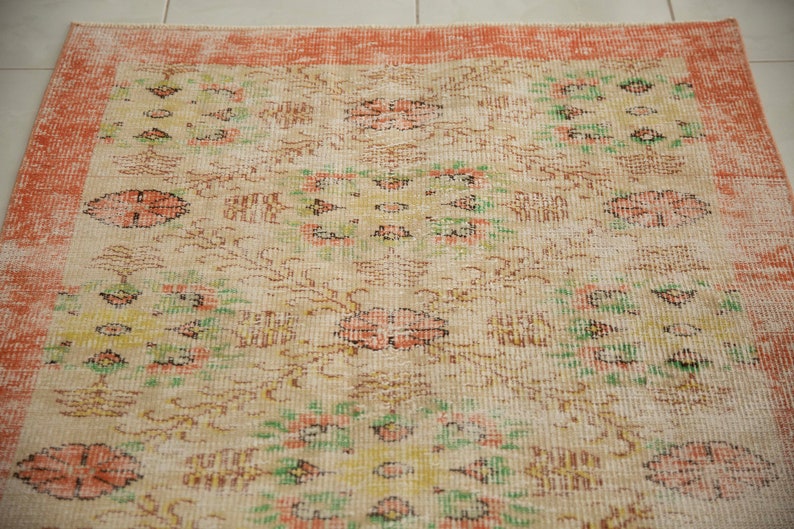 May include: A vintage rug with a cream background and a peach border. The rug has a floral pattern with green, peach, and brown accents.