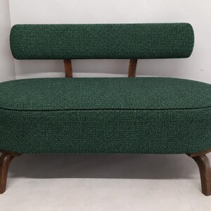 May include: A small loveseat upholstered in a textured dark green fabric. The piece features an oval-shaped seat, a rectangular backrest supported by two wooden struts, and four curved wooden legs with a dark brown finish.