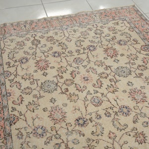 May include: A vintage rug with a cream background and a floral pattern in shades of pink, blue, and gray. The rug has a border with a repeating pattern of pink and gray.