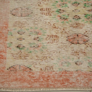 May include: A vintage rug with a cream background and a floral pattern in shades of brown, green, and pink. The rug has a peach-colored border and a fringe edge.