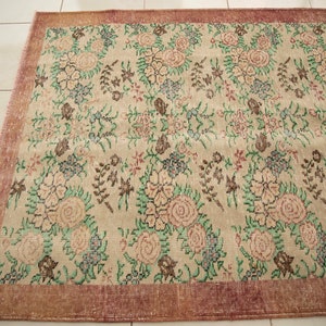 May include: A vintage rug with a floral pattern in shades of pink, green, and brown. The rug has a cream background and a reddish-brown border.