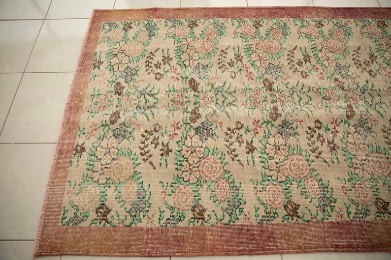 May include: A vintage rug with a floral pattern in shades of pink, green, and brown. The rug has a cream background and a reddish-brown border.