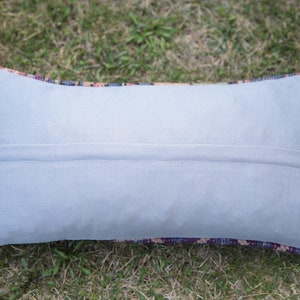 May include: A light gray rectangular pillow with a zipper closure. The pillow is made of a soft, smooth fabric and has a subtle sheen. The pillow is lying on a bed of green grass.