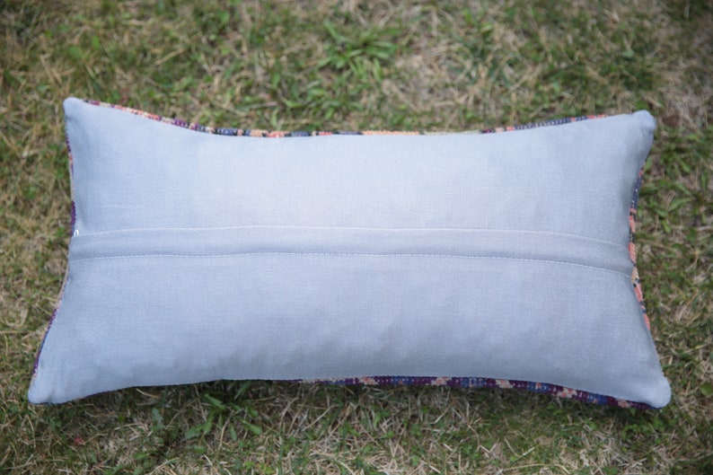 May include: A light gray rectangular pillow with a zipper closure. The pillow is made of a soft, smooth fabric and has a subtle sheen. The pillow is lying on a bed of green grass.