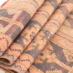 May include: A folded rug with a geometric pattern in shades of pink, brown, and gray. The rug has a fringe border.