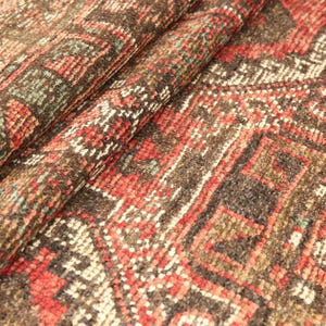 a close-up view of a colorful, intricately patterned rug or carpet with a variety of geometric shapes and designs in shades of red, orange, and brown.
