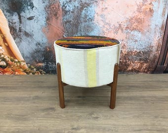 May include: A round, white and yellow striped ottoman with a dark patterned top. The ottoman has four wooden legs.