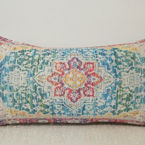 May include: A rectangular throw pillow with a colorful, intricate patterned design. The pattern features a central floral motif in shades of red, yellow, and blue, surrounded by a border of smaller floral designs. The pillow is made of a soft, textured fabric.