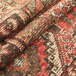 a close-up view of a colorful, intricately patterned rug or carpet with a variety of geometric shapes and designs in shades of red, orange, and brown.