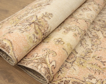 Puede incluir: Una alfombra vintage con un patrón floral en tonos beige, marrón y crema. La alfombra está doblada por la mitad, mostrando los intrincados detalles del diseño.