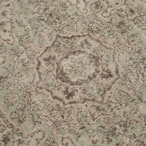 K&ouml;nnte beinhalten: Ein Vintage-Teppich mit einem verblassten gr&uuml;n-braunen Blumenmuster. Der Teppich hat einen abgenutzten Look und ist aus einem weichen, gewebten Material gefertigt.