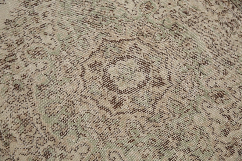 K&ouml;nnte beinhalten: Ein Vintage-Teppich mit einem verblassten gr&uuml;n-braunen Blumenmuster. Der Teppich hat einen abgenutzten Look und ist aus einem weichen, gewebten Material gefertigt.