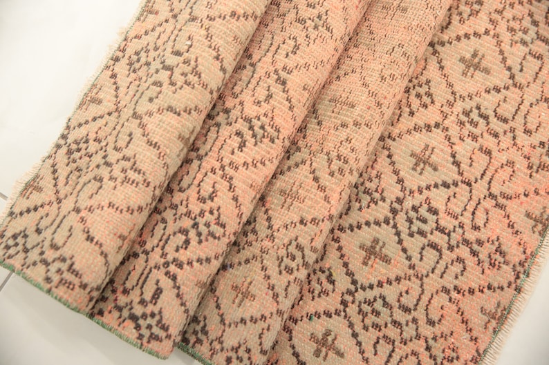 May include: A folded pink and brown patterned rug with a green fringe. The rug has a floral design.