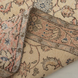 May include: Close-up of the edge of a beige rug with a floral pattern. The rug has a fringe border and is woven with intricate details.
