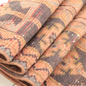 May include: Close-up of a folded rug with a geometric pattern in shades of pink, brown, and gray.