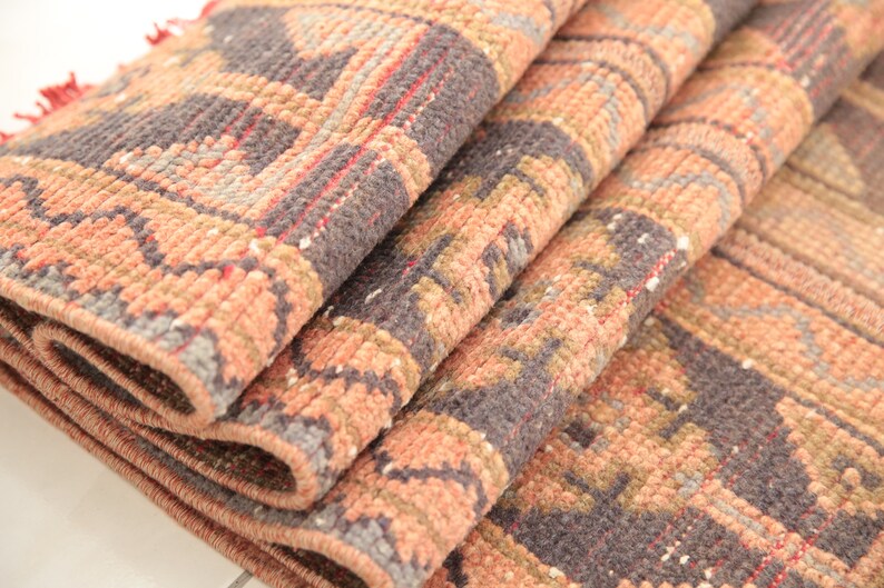 May include: Close-up of a folded rug with a geometric pattern in shades of pink, brown, and gray.