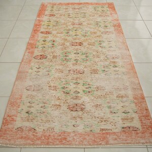 May include: A vintage runner rug with a floral pattern in shades of pink, green, and cream. The rug has a distressed look and a faded, vintage aesthetic.
