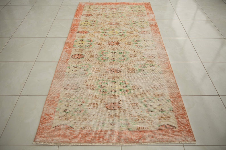 May include: A vintage runner rug with a floral pattern in shades of pink, green, and cream. The rug has a distressed look and a faded, vintage aesthetic.