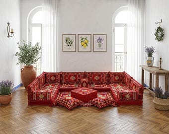 Puede incluir: Un sofá seccional rojo con un diseño estampado, acompañado de cojines a juego y una otomana cuadrada. La habitación cuenta con estampados botánicos enmarcados, un jarrón grande de terracota y una mesa auxiliar de madera con un jarrón de lavanda.