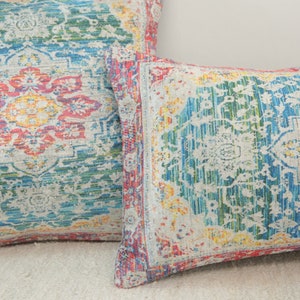 May include: Two decorative throw pillows with a colorful, intricate floral pattern. The pillows are made of a soft, textured fabric and feature a white background with shades of blue, green, yellow, and red.