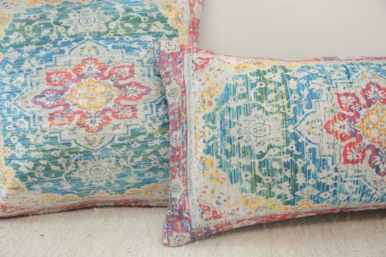 May include: Two decorative throw pillows with a colorful, intricate floral pattern. The pillows are made of a soft, textured fabric and feature a white background with shades of blue, green, yellow, and red.