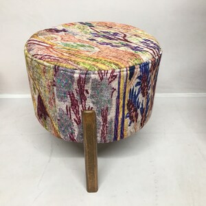 May include: A colorful patterned footstool with a wooden base. The footstool has a round top and three legs.