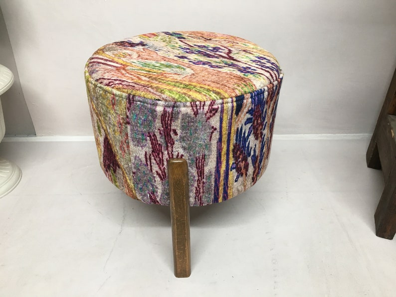 May include: A colorful patterned footstool with a wooden base. The footstool has a round top and three legs.