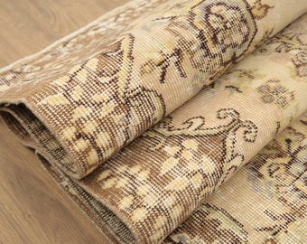 Könnte beinhalten: Ein beige-brauner Teppich mit floralem Muster. Der Teppich ist in der Mitte gefaltet und die Kanten sind sichtbar.