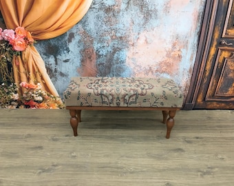 Puede incluir: Un pequeño banco de madera con un asiento de tela estampada. El banco tiene patas torneadas y está delante de una pared texturizada con una cortina.