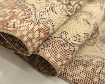 Puede incluir: Primer plano de una alfombra enrollada de color beige y marrón con estampado. La alfombra tiene un diseño tradicional con detalles intrincados.
