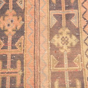 May include: A close-up of a vintage rug with a geometric pattern in shades of brown, beige, and pink. The rug has a fringe border and is woven with intricate details.