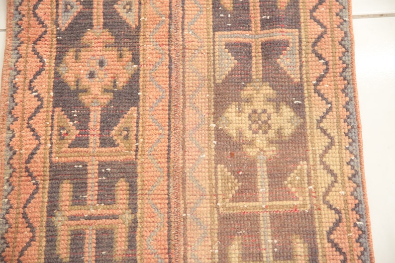 May include: A close-up of a vintage rug with a geometric pattern in shades of brown, beige, and pink. The rug has a fringe border and is woven with intricate details.