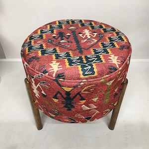 Puede incluir: Un puf redondo de color rojo, negro y amarillo con un marco de madera. El puf tiene un dise&ntilde;o geom&eacute;trico con figuras estilizadas.