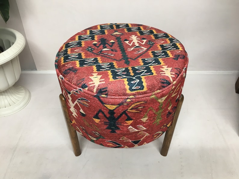 Puede incluir: Un puf redondo de color rojo, negro y amarillo con un marco de madera. El puf tiene un dise&ntilde;o geom&eacute;trico con figuras estilizadas.