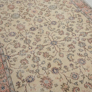 May include: A vintage cream-colored rug with a floral pattern in shades of pink, blue, and brown. The rug has a border with a repeating pattern of pink and brown.